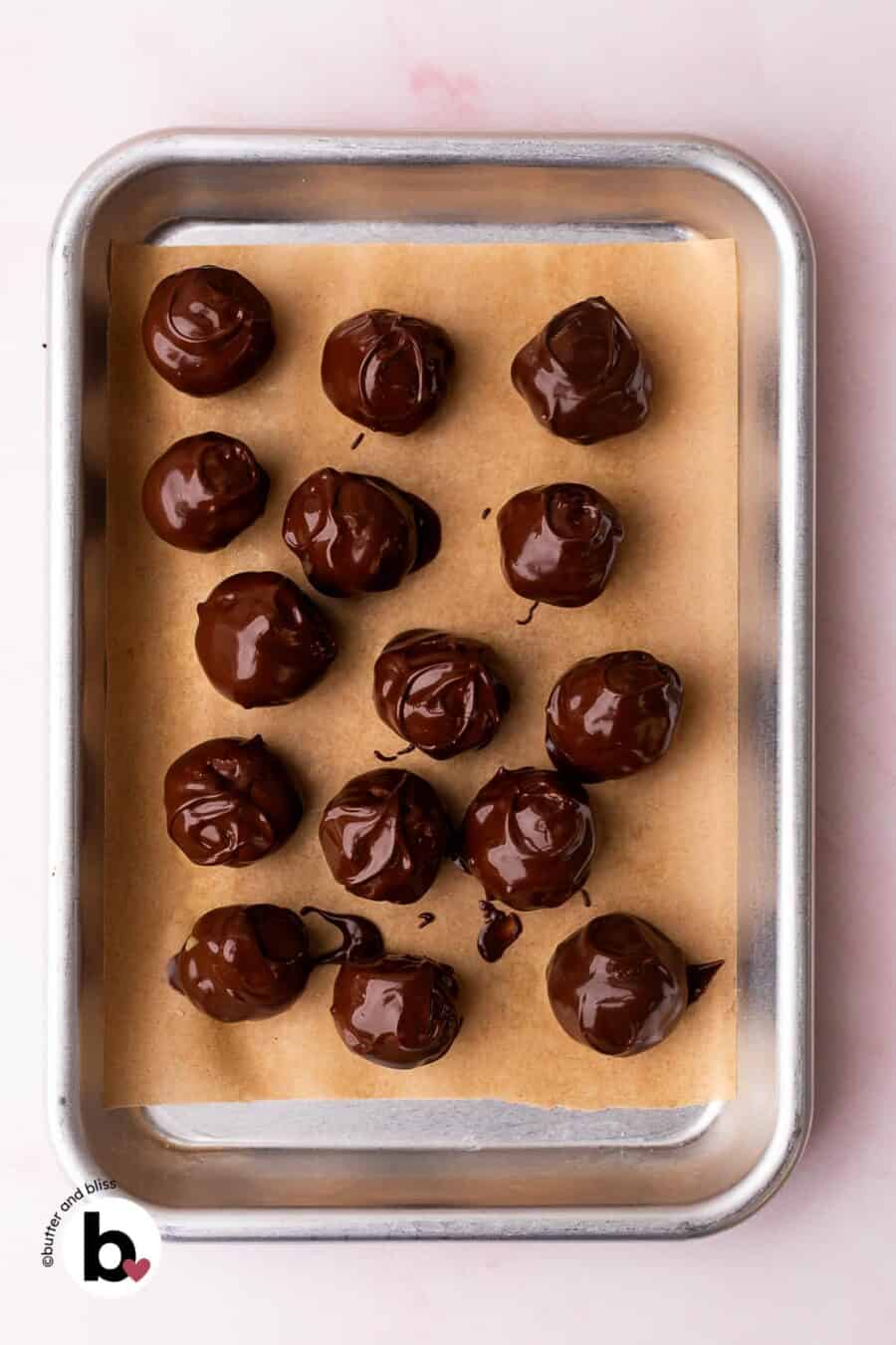 Edible cookie dough bites just dipped into melted chocolate on a baking sheet.