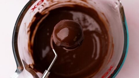 Hand holding a chocolate dipped cookie dough bite over a bowl of melted chocolate.