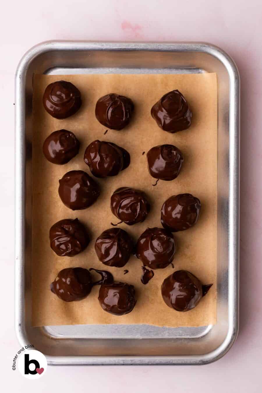 Edible cookie dough bites just dipped into melted chocolate on a baking sheet.