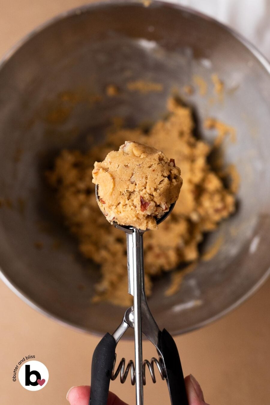 Hand holding a cookie scoop full of maple brown sugar cookie dough.