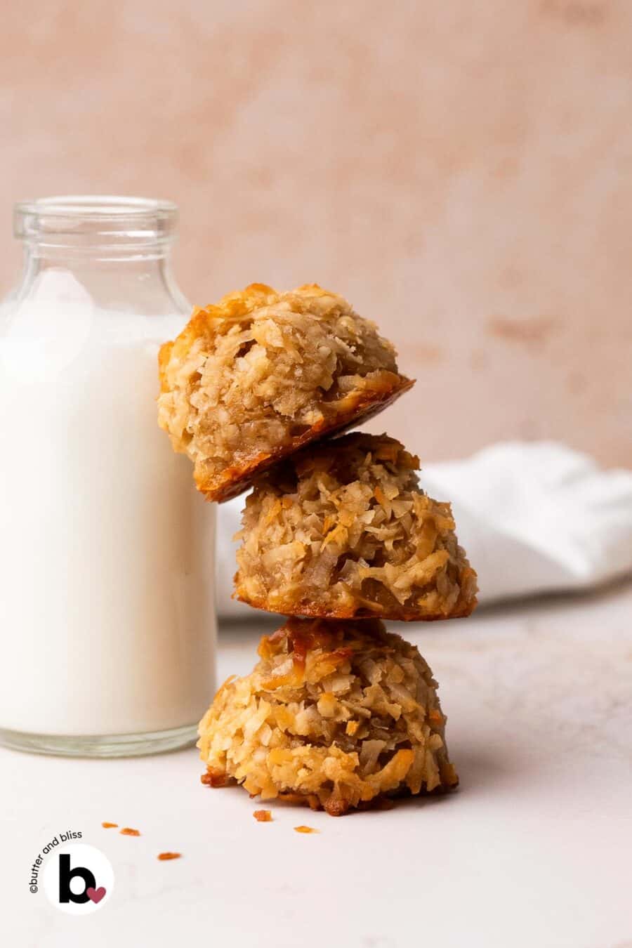 Three coconut maple macaroons stacked next to a glass of milk.