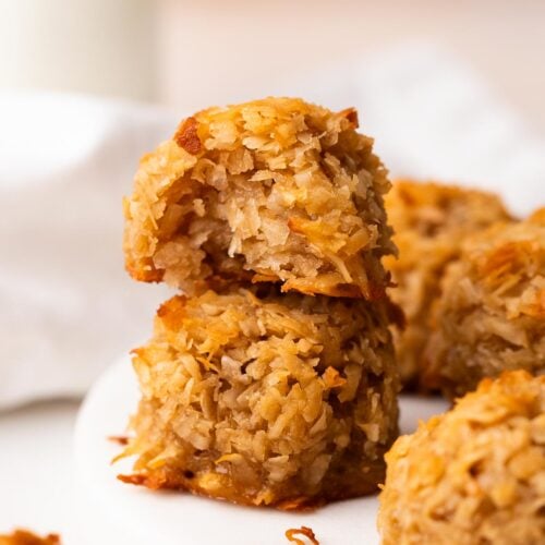 Two coconut maple macaroons stacked on a white plate with a bite taken out of one.