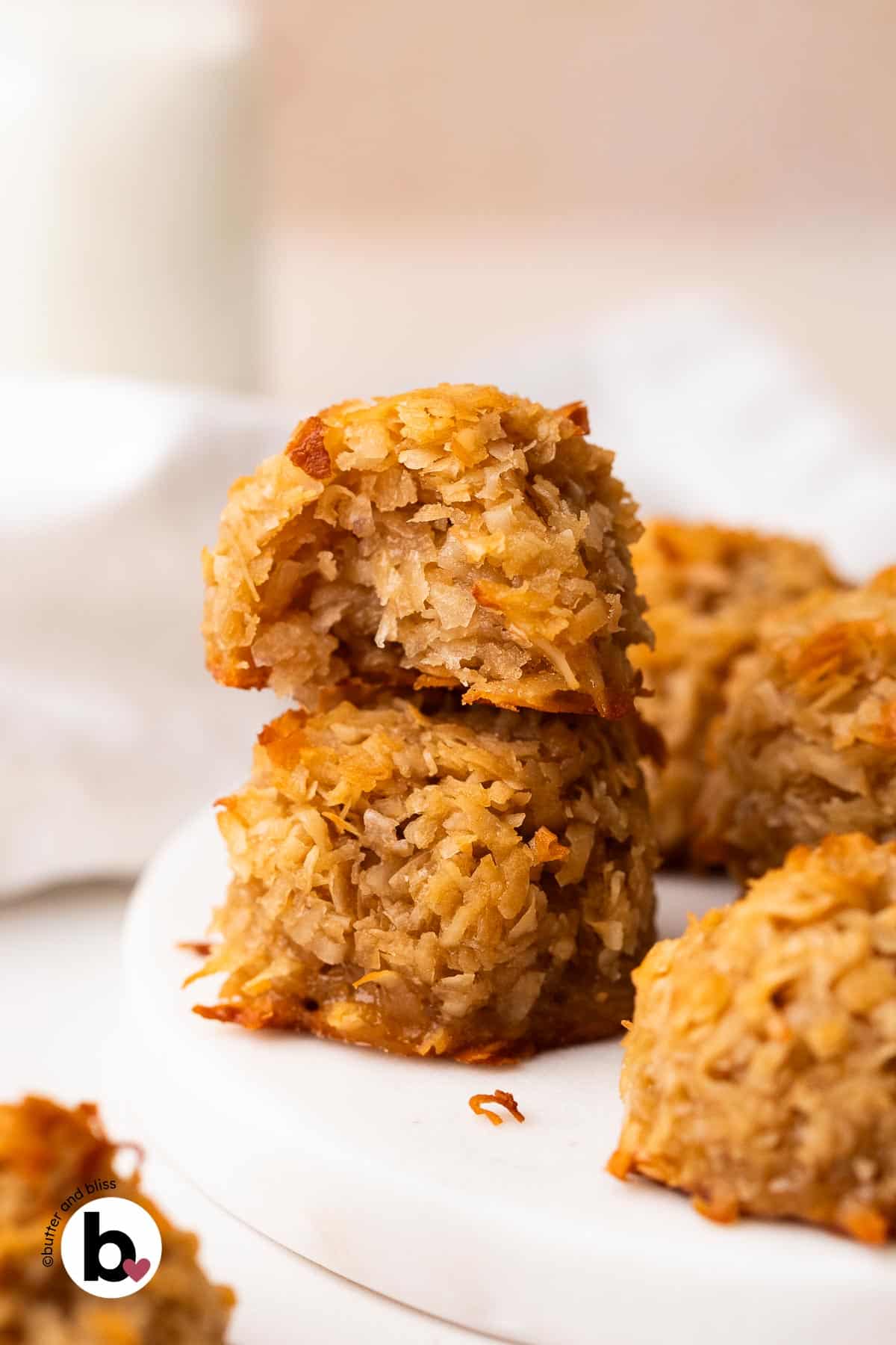 Two coconut maple macaroons stacked on a white plate with a bite taken out of one.