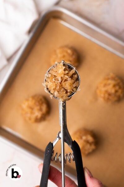 Hand holding a cookie scoop full of maple macaroons dough.