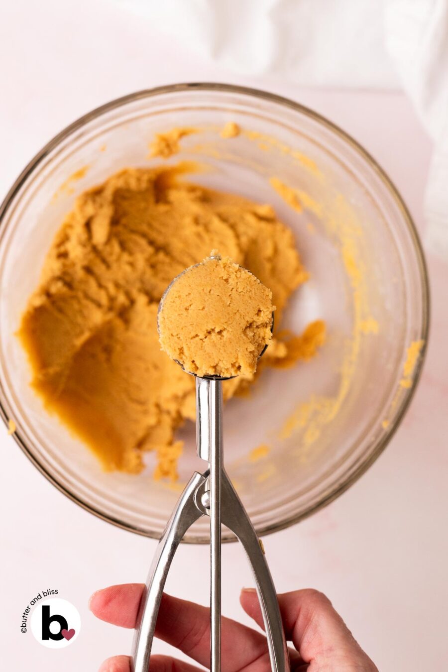 Hand holding a cookie scoop full of peanut butter cookie dough.