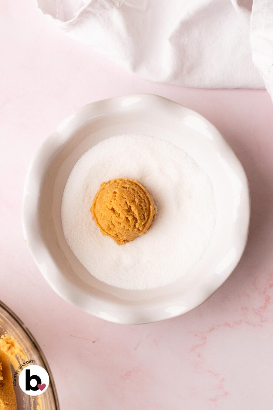 Peanut butter blossom cookie dough ball rolled in a bowl of white sugar.