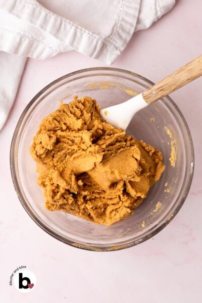 Thick peanut butter blossom cookie dough in a mixing bowl with a white whisk.