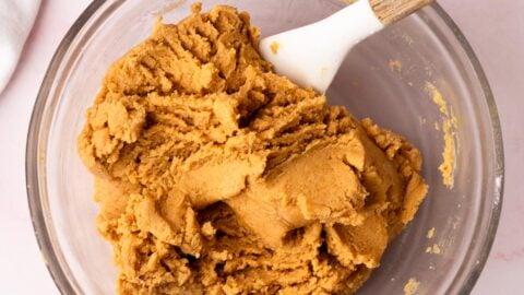Thick peanut butter blossom cookie dough in a mixing bowl with a white whisk.