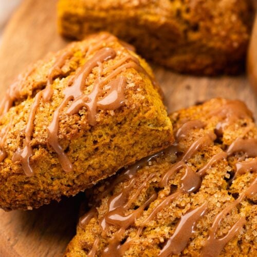Two pumpkin scones drizzled with cinnamon glaze, stacked on a wood plate.