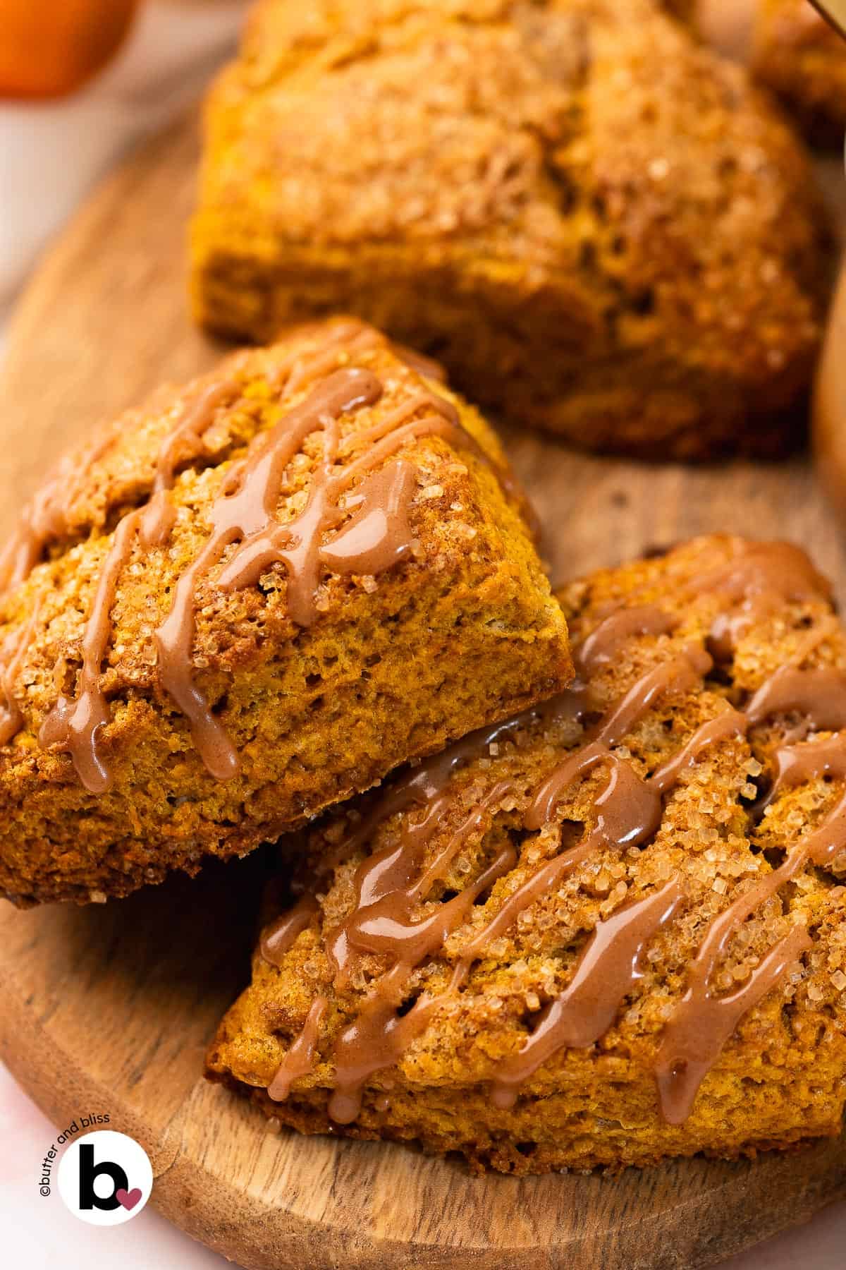 Two pumpkin scones drizzled with cinnamon glaze, stacked on a wood plate.