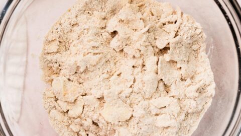 Flaky discs of butter mixed into dry ingredients in a mixing bowl.
