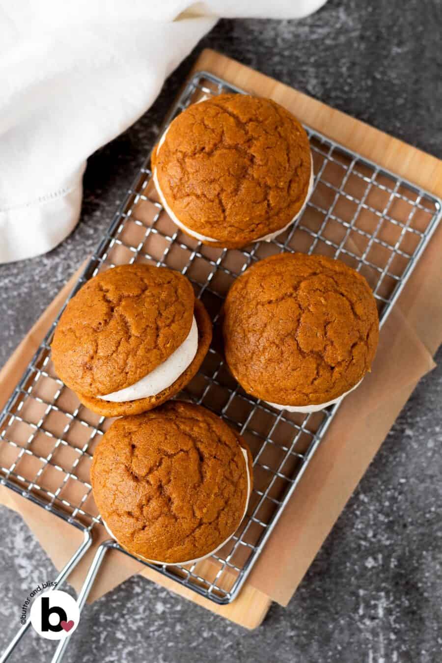Assembled pumpkin whoopie pies with cream cheese filling on a wire rack.