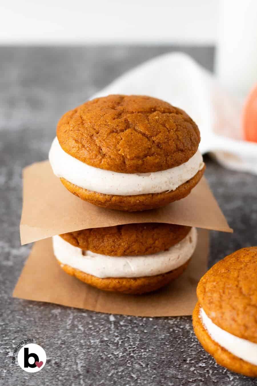 Two cream cheese frosting filled pumpkin whoopie pies stacked on a table.