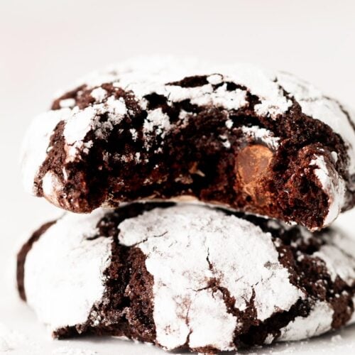 Two chocolate crinkle cookies stacked on a table with a bite out of one.