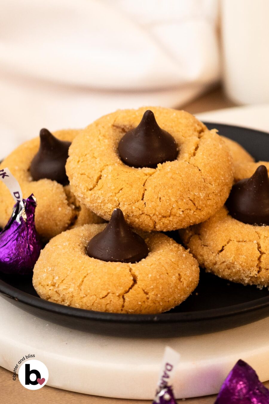 A black plate of peanut butter blossom cookies, surrounded by Hershey's kissses.